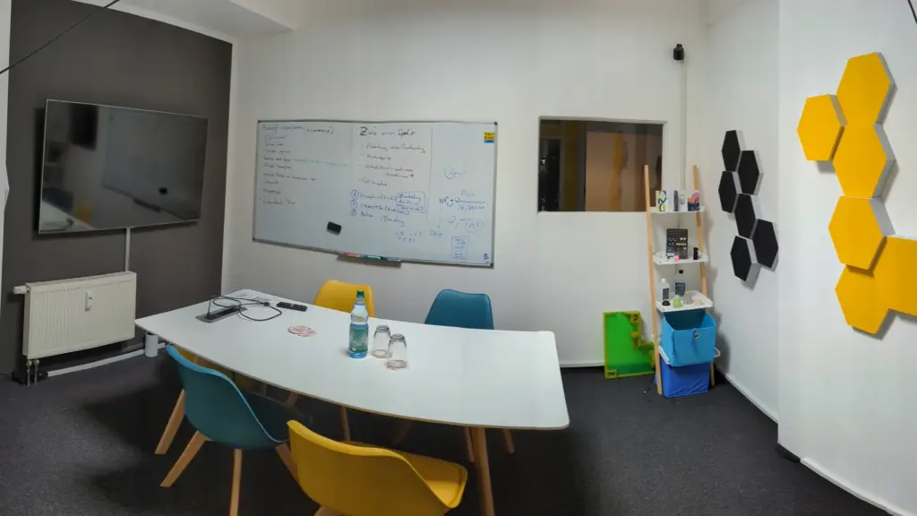 Kleiner Meetingraum mit Whiteboard, Bildschirm und gelben Akustikwaben